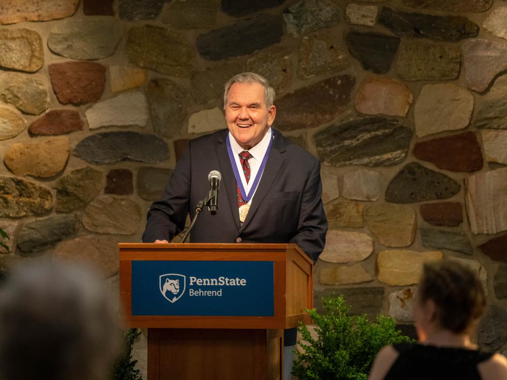 Former Gov. Tom Ridge smiles while standing at a podium at Penn State Behrend.