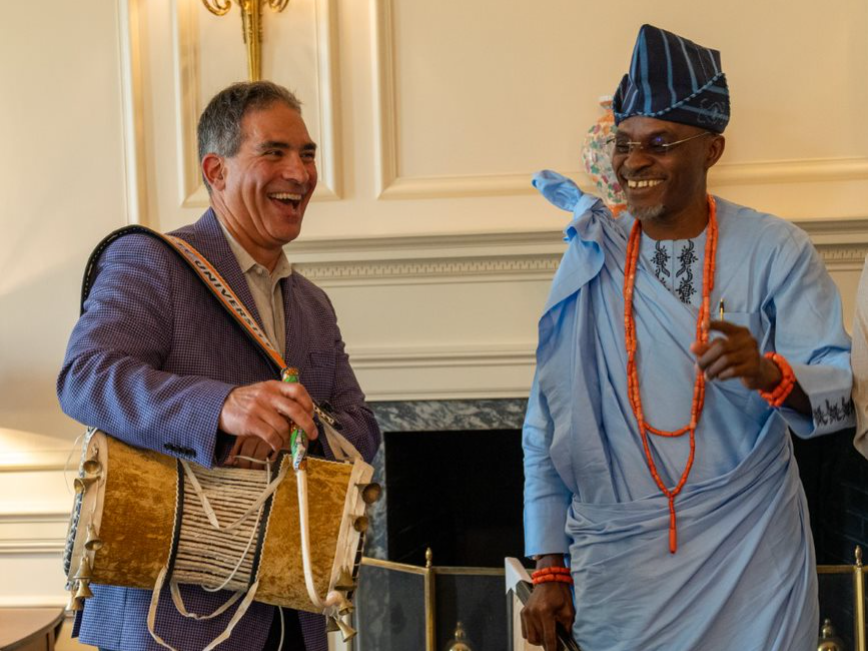 Two men standing next to each other, one holding a drum and laughing