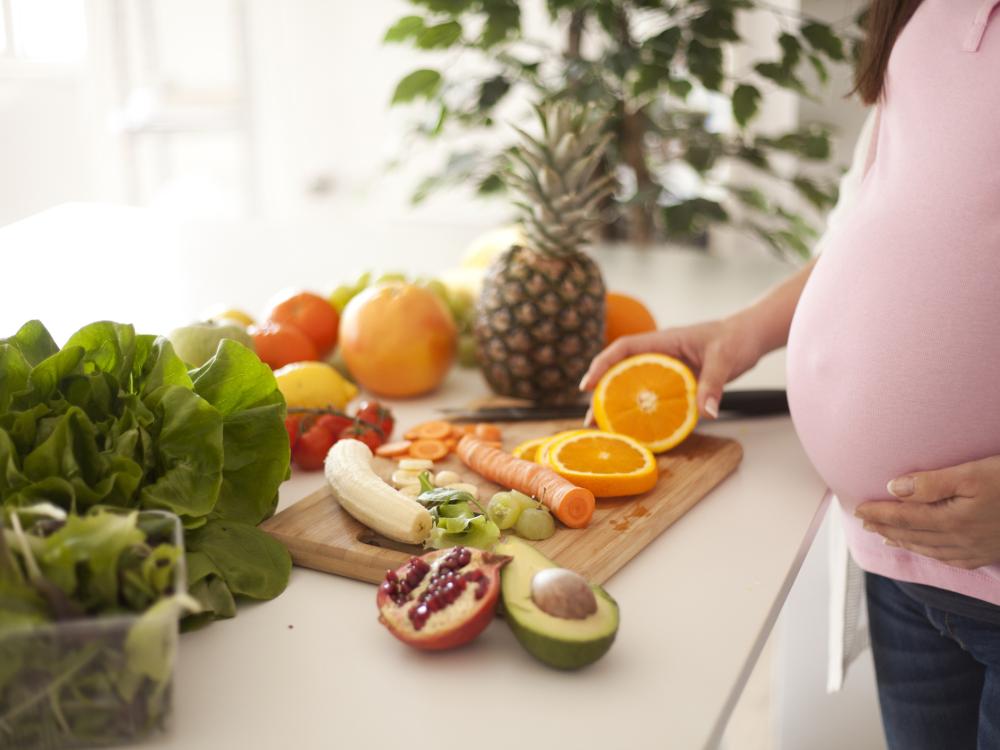 Torso of a pregnant woman in front of counter with an array of fresh fruits and vegetables