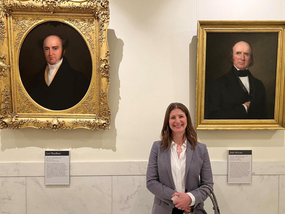 Rachel Shelden stands in front of paintings of Supreme Court justices