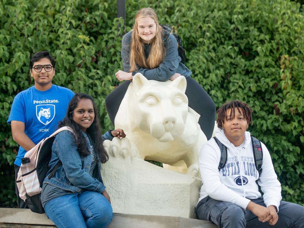 Four students, two males and two females, sitting on and around the Nittany Lion Shrine