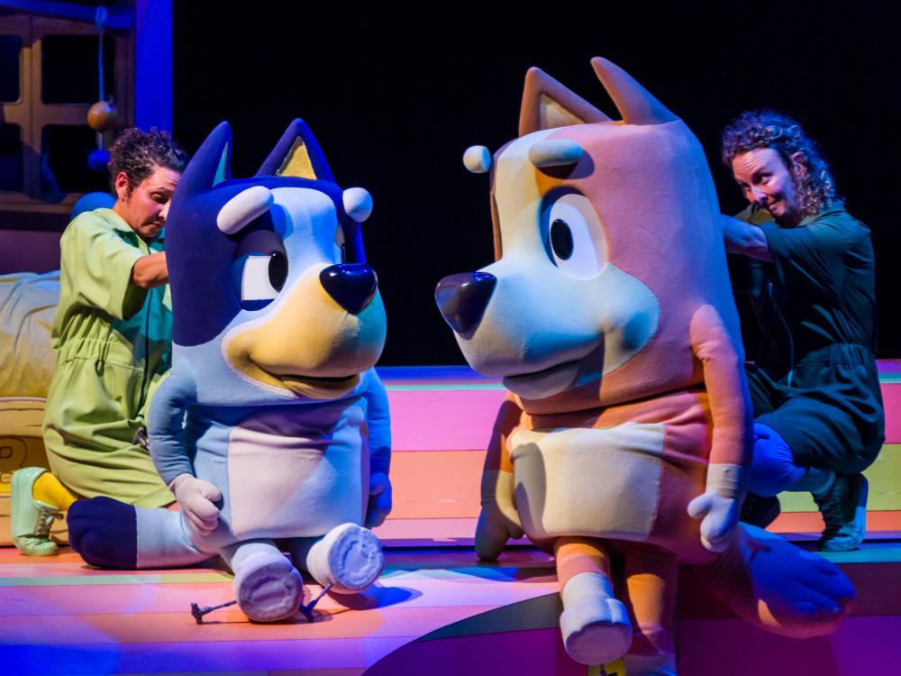 Puppeteers stand behind two oversized cartoonish dogs.
