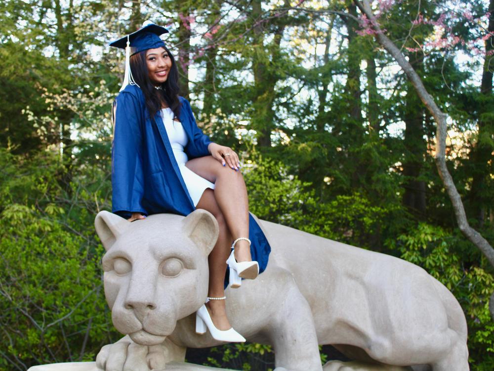 Donned in cap and gown, Jaelyn Monroe sits on the Nittany Lion Shrine at Penn State University Park.