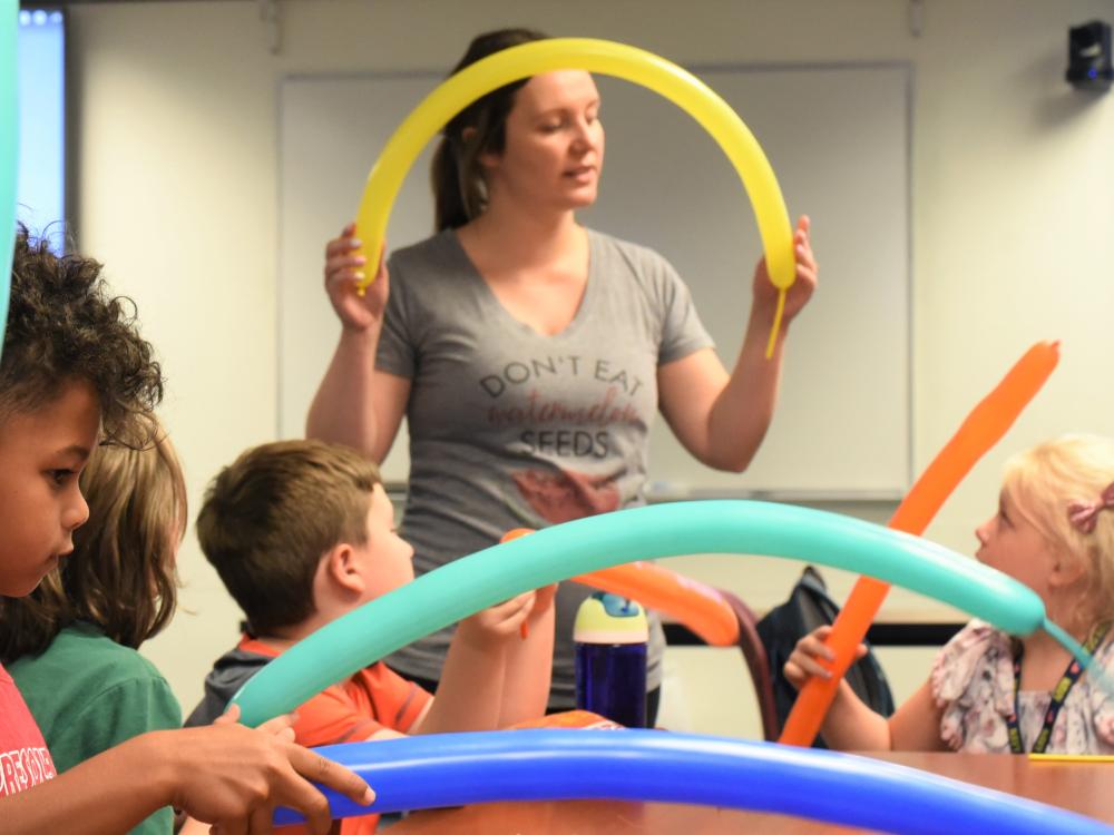 A female instructor bends a long balloon during a youth summer class about the Macy's Thanksgiving Day parade.