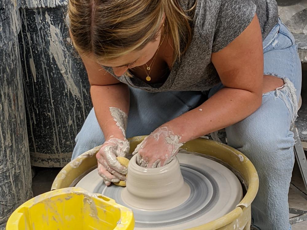 A student spinning a wheel of pottery during a class