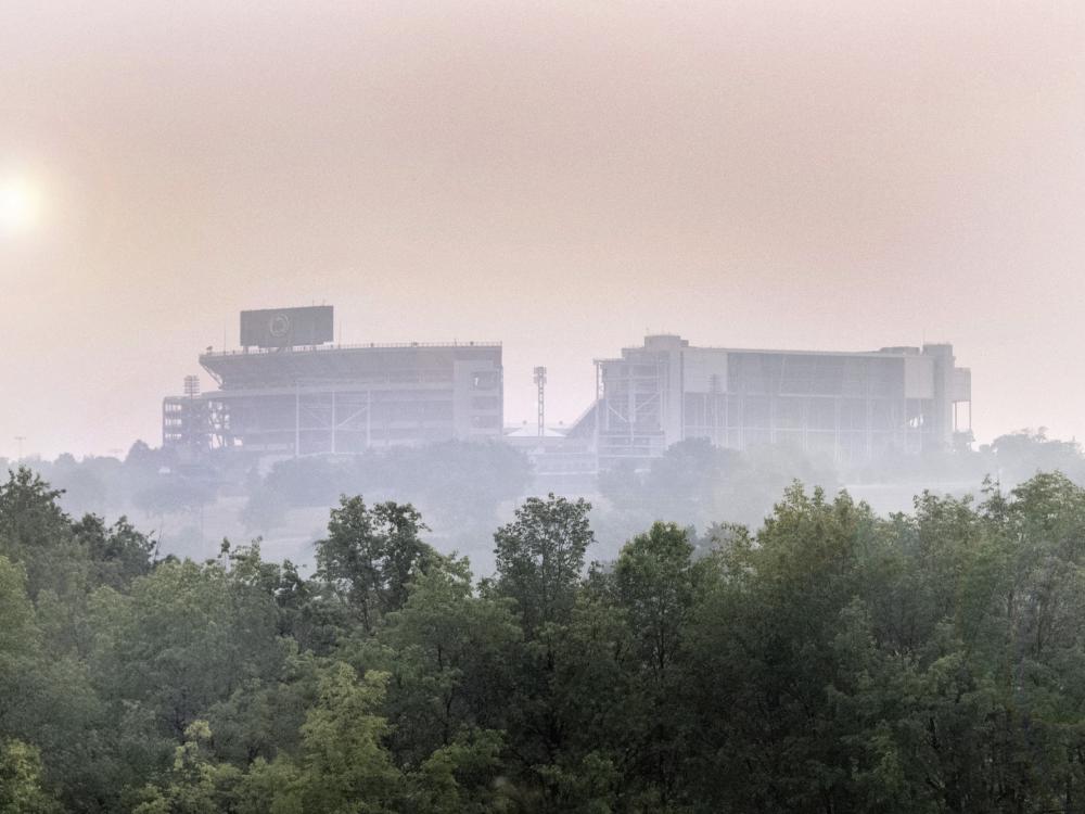 Beaver Stadium shrouded by smoke from Canadian wildfires, with trees in the foreground