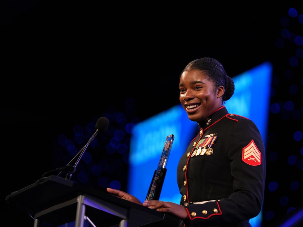A woman wearing a military uniform speaks at a podium.