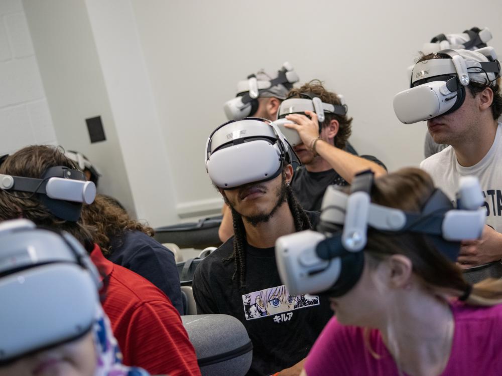 Students in a classroom wear white reality headsets that cover their eyes