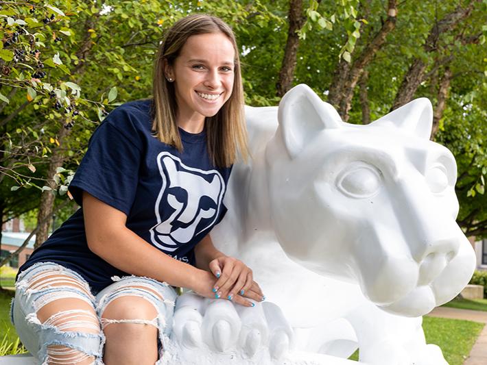 Alexis sits at the Lion Shrine on the Beaver campus wearing a navy and white Lion Ambassadors t-shirt.