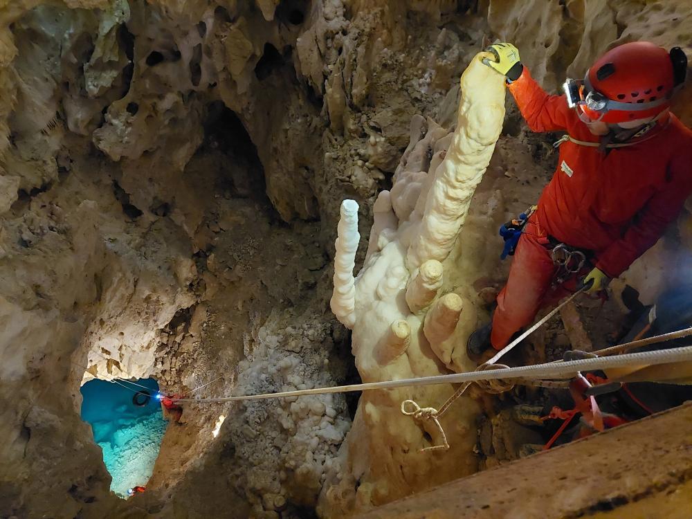 A caver peers down a large drop into an underground lake