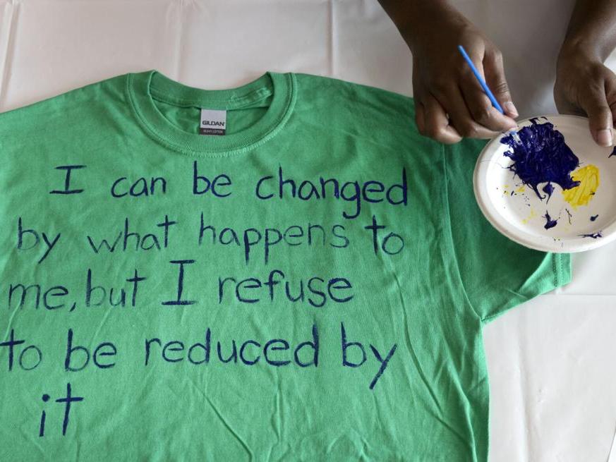 A green t-shirt with painted words reading I can be changed by what happens to me but I refuse to be reduced by it 