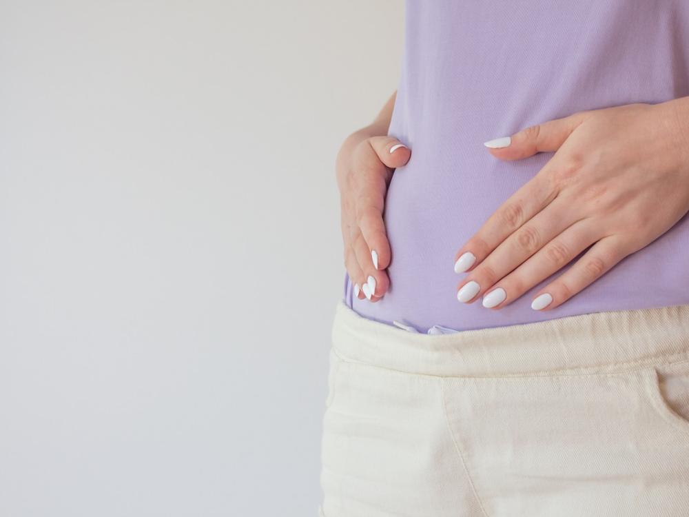 A pregnant person holds their hands over their abdomen. 