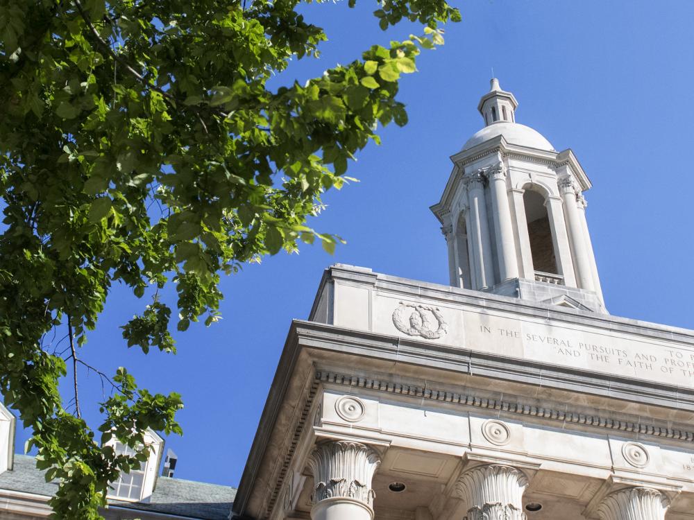 The tower of Old Main building above the trees against a brilliant blue sky