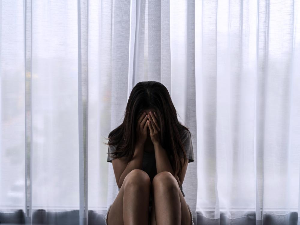 A woman sitting in front of a window with her face in her hands.
