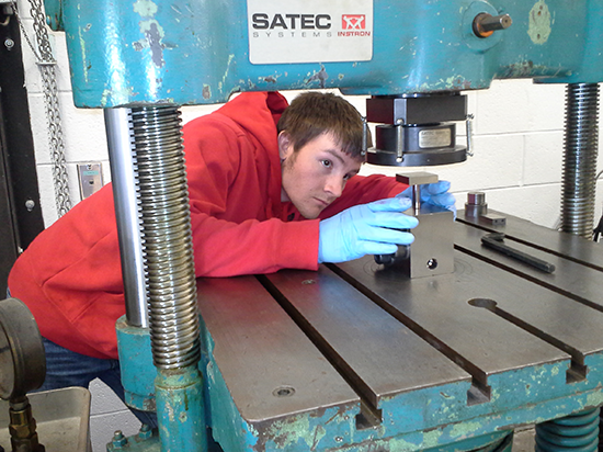 Person in a red hoodie and blue gloves works with a metal machine