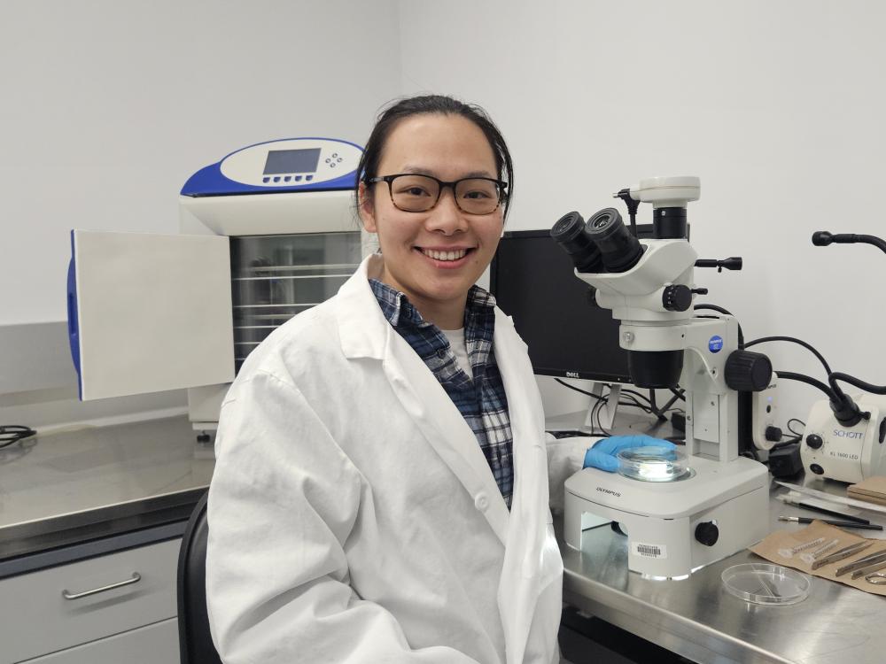 Person wearing a lab coat standing in front of a microscope