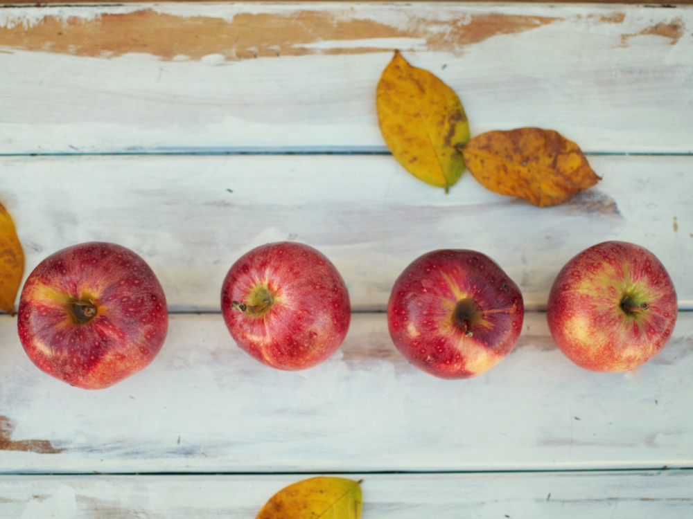 Four apples lined up on a wooden table