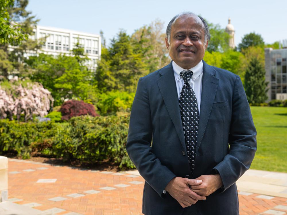 A person in a suit and tie stands outside and smiles at the camera