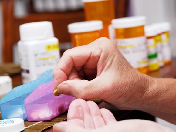 A woman’s hand shown filling pill boxes, with prescription bottles in the background.