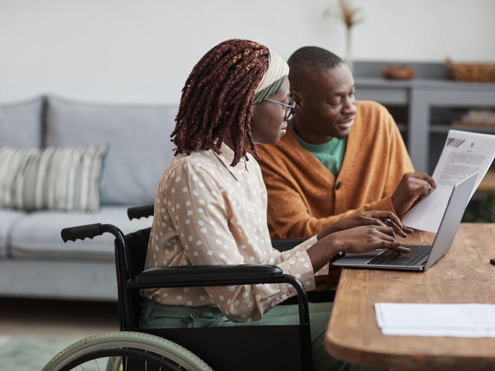 two people, one in a wheelchair, look at a laptop