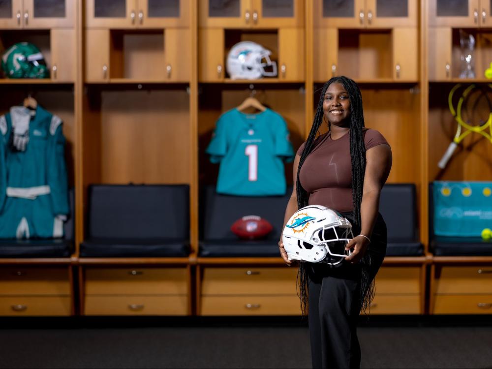 Azziyah LaRue holds a Miami Dolphins football helmet in the Miami Dolphins locker room at Hard Rock Stadium. 