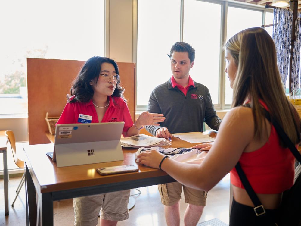 Two student orientation leaders at a check-in table helping a new student