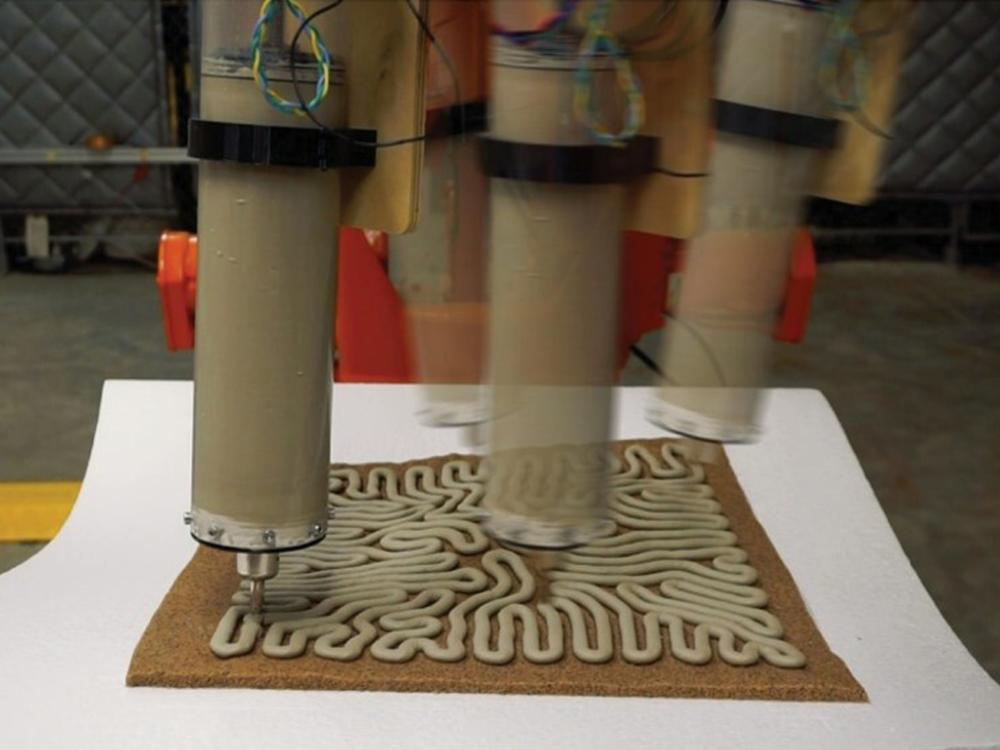 A time-lapse image showing a robotic arm extruding a concrete substance as it 3D prints a structure. 