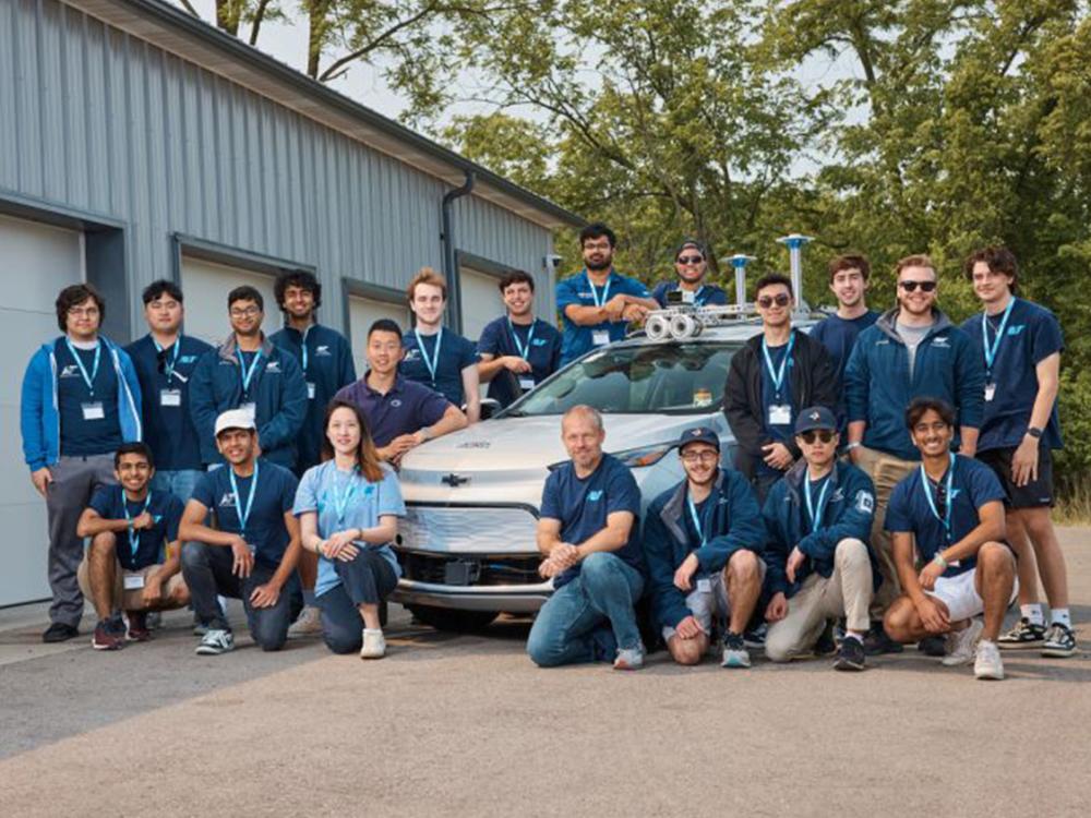 Team members pose for a picture with their autonomous vehicle in front of a garage