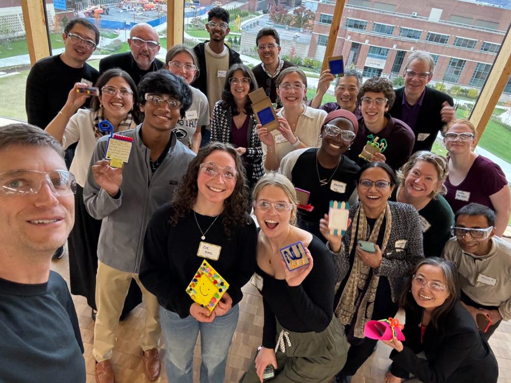 A group photo of people smiling and holding up small projects. 