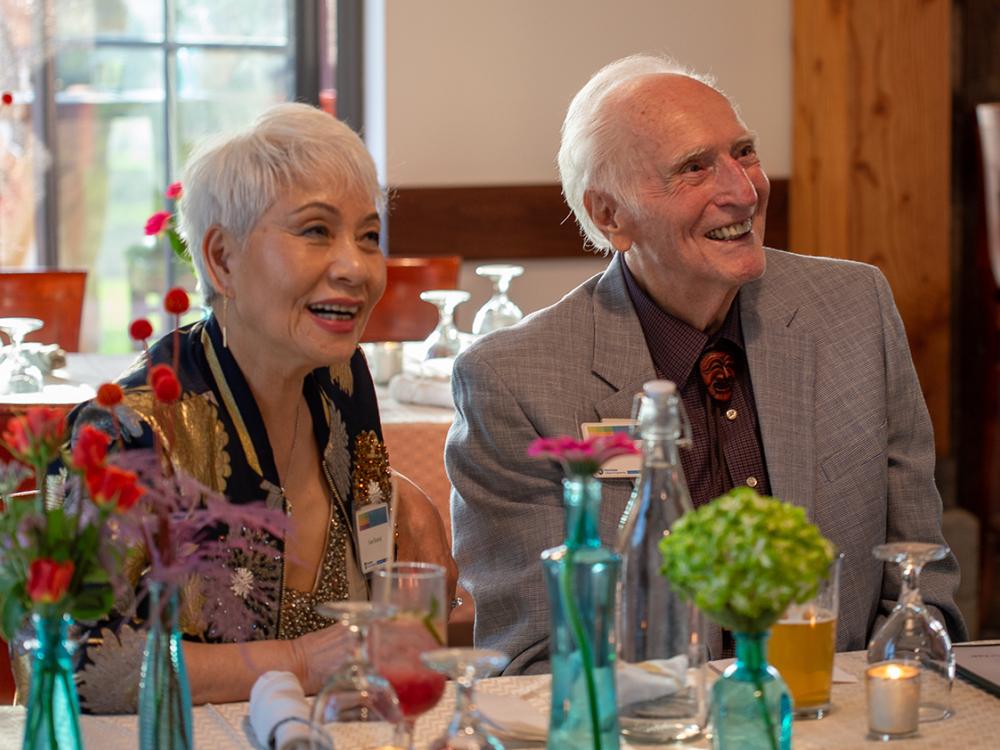 Two smiling individuals sit at a table in a restaurant.