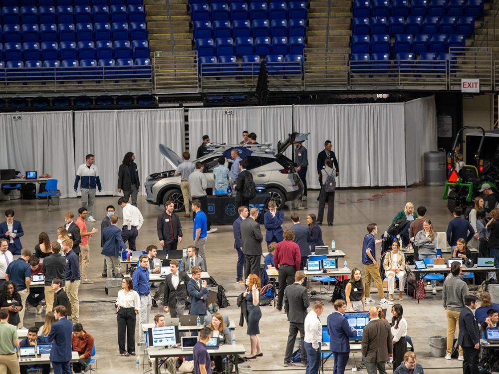 Students walk around tables and a car that are on the floor of the Bryce Jordan Center.