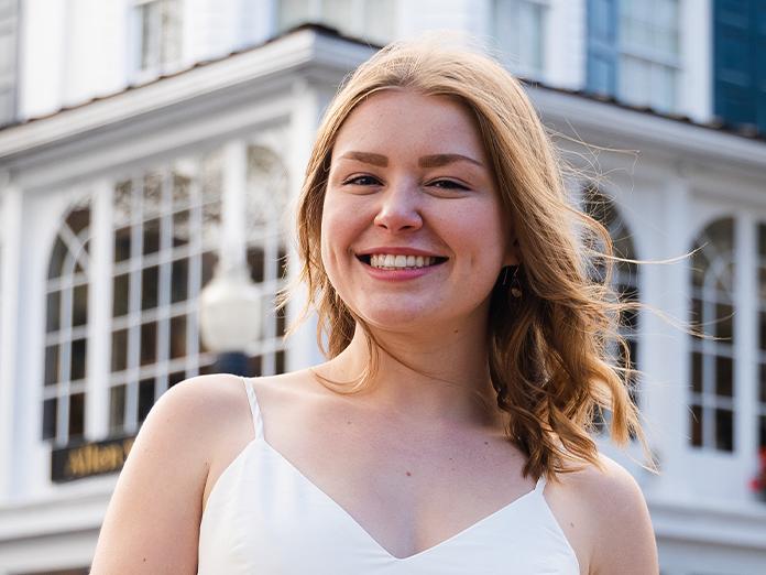 Red-haired young woman in a white sun dress smiling outside. 