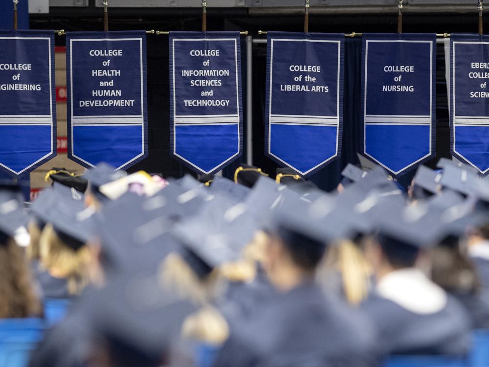 A group of people wear blue graduation caps and gowns during a ceremony.