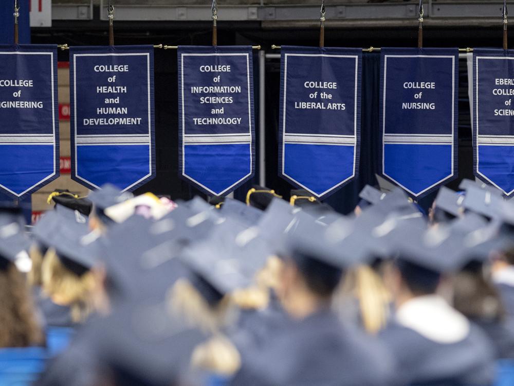A group of people wear blue graduation caps and gowns during a ceremony.