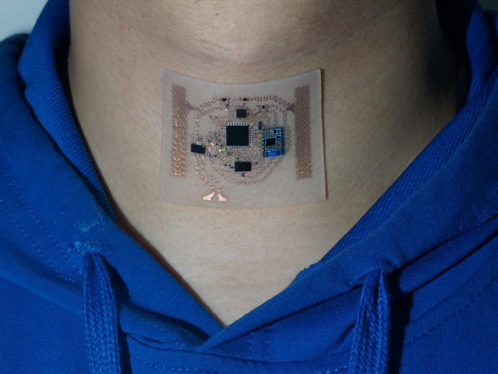 A wearable medical sensor is seen on an individual's neck.