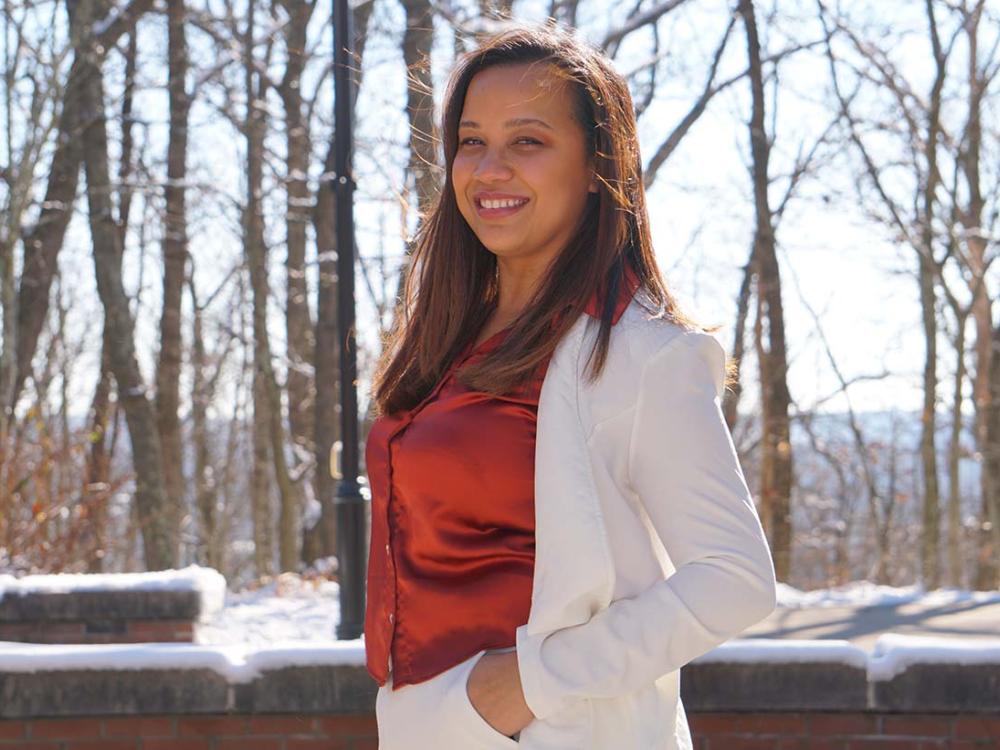 Woman dressed in business casual, white pantsuit, outdoors with snow and trees in background. 