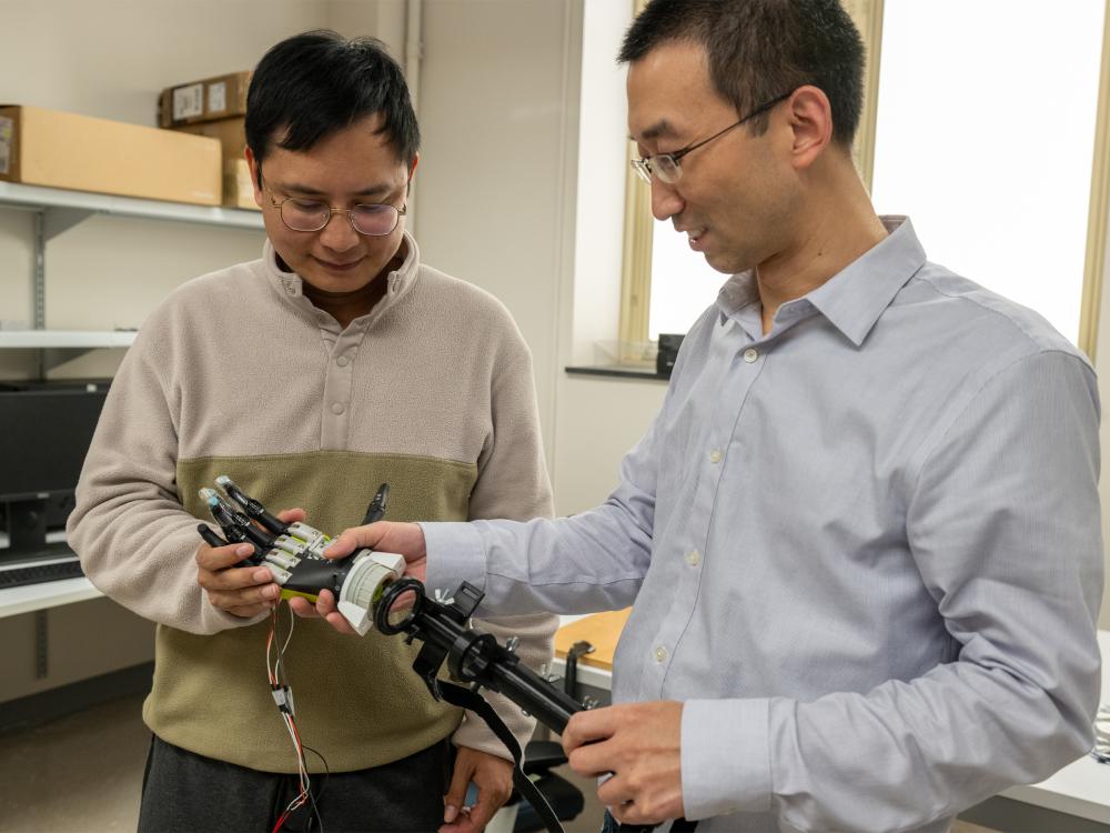 Two individuals look down at a robotic arm.