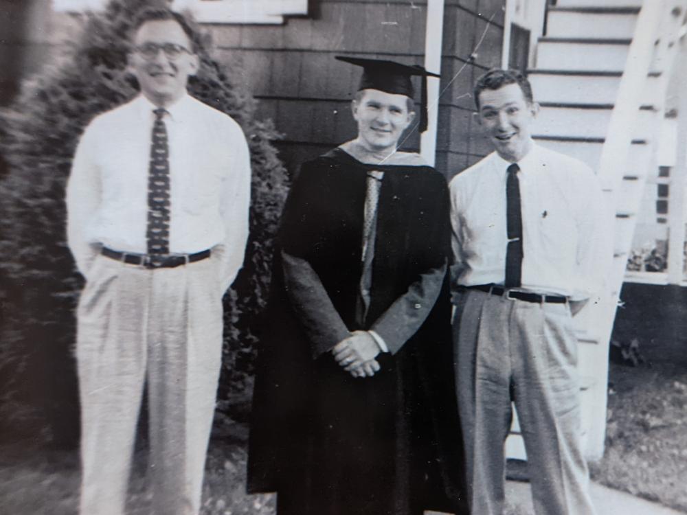 A black-and-white photo of three brothers, one wearing a cap and gown, posing outdoors.  