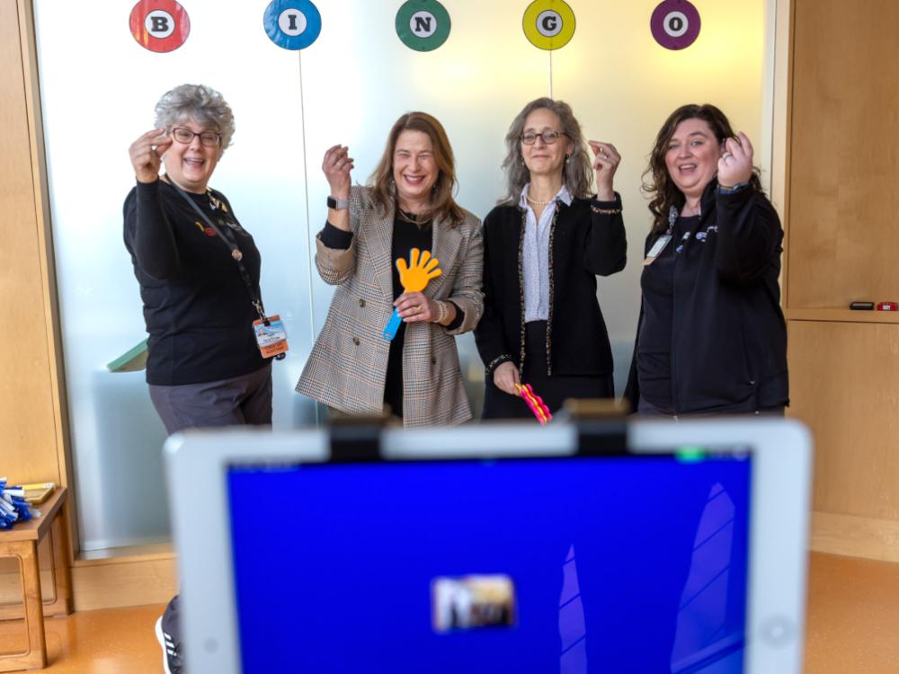 Four women stand in front of a screen, playing bingo
