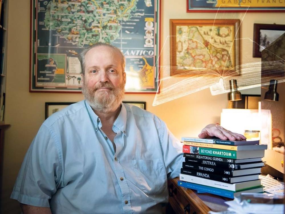 Randall Fegley sits at desk with books on top of it