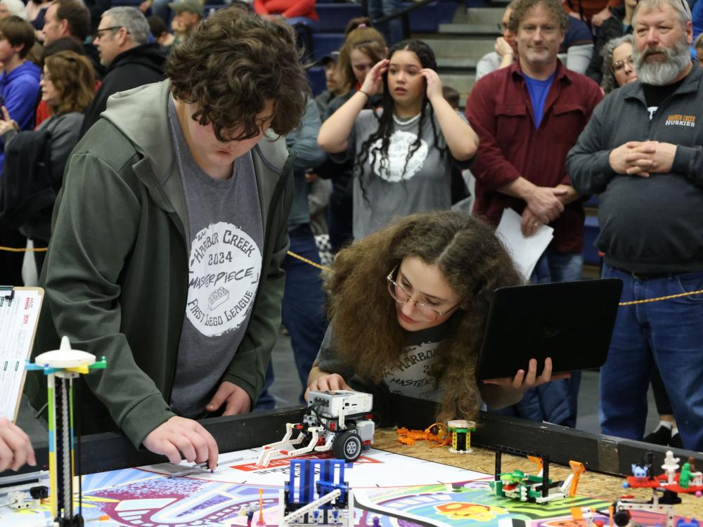 A student and a teacher check a robot on a tabletop obstacle course.