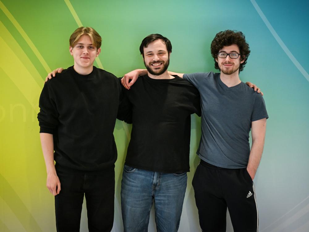 Three people pose for a photo in fron of the backdrop of a colorful wall