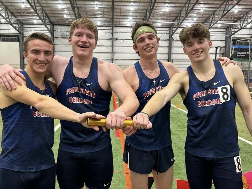 Four Penn State Behrend runners pose while holding a track baton.