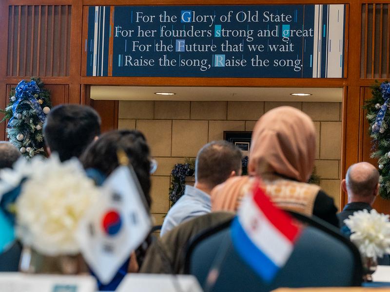 Two table flags in the foreground with a plaque of Penn State's Alma Mater in the background