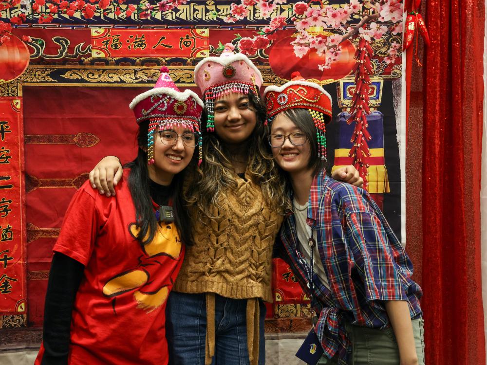 three students posing for photo with a Chinese new year backround of red and gold