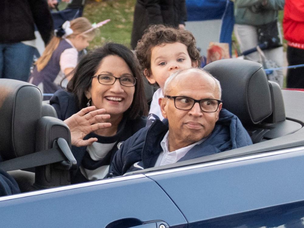 Neeli and Venkat Bendapudi wave from the back of a car in Penn State's homecoming parade