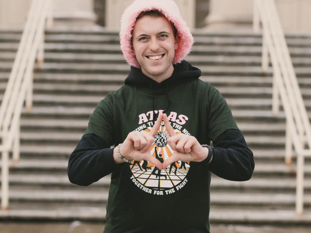 Young man with a pink, fuzzy hat standing in front of Old Main