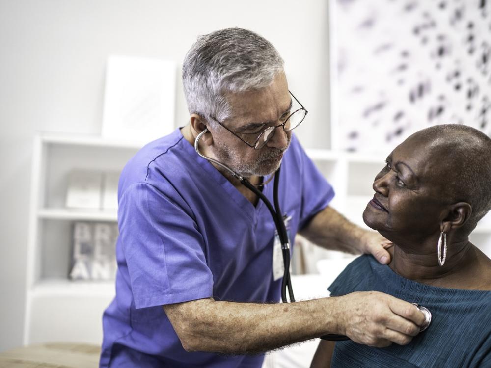 A doctor uses a stethoscope to listen to the heartbeat of an older patient.