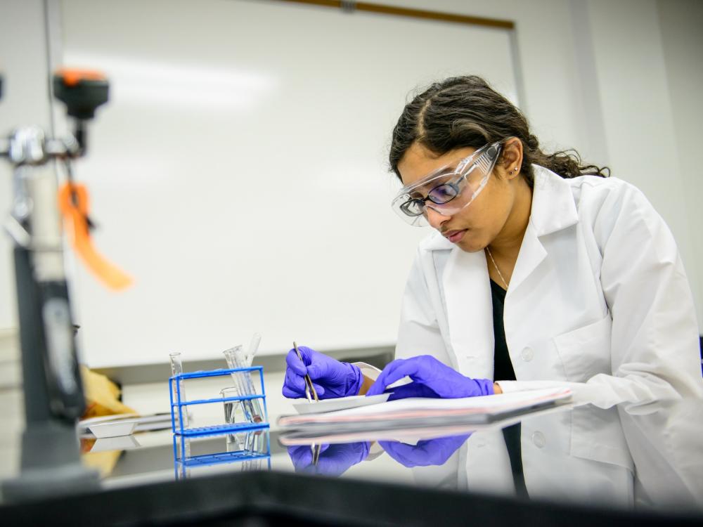 Individual performing laboratory experiment with white lab coat, safety glasses, and gloves.