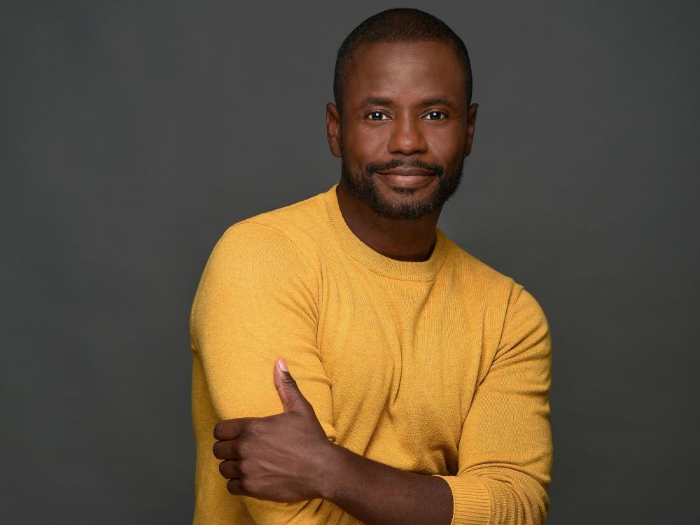 Black man with a yellow sweater posing casually